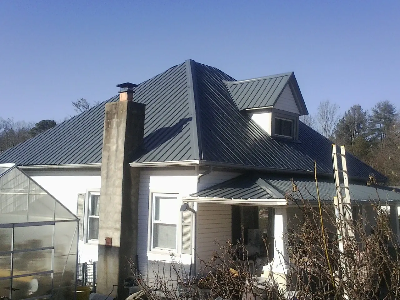 Dark blue standing seam metal roof on a white farmhouse with dormer — Slate & Tile Roof Repair by Roofing Brothers in Cranford