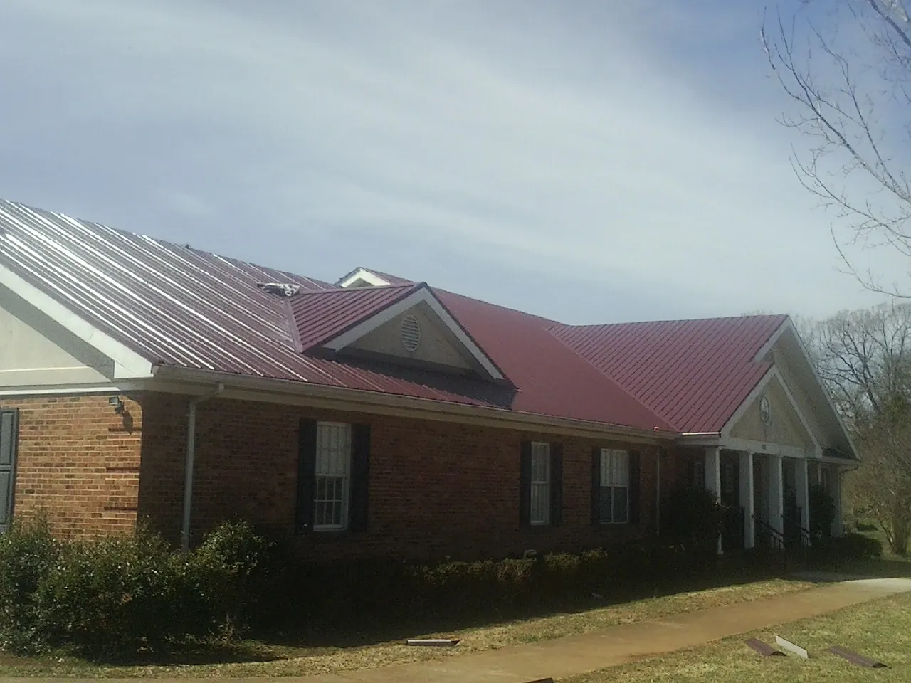 Red metal roof with gabled entries on a long brick building, from a Hail Damage Roof Repair job in Cranford