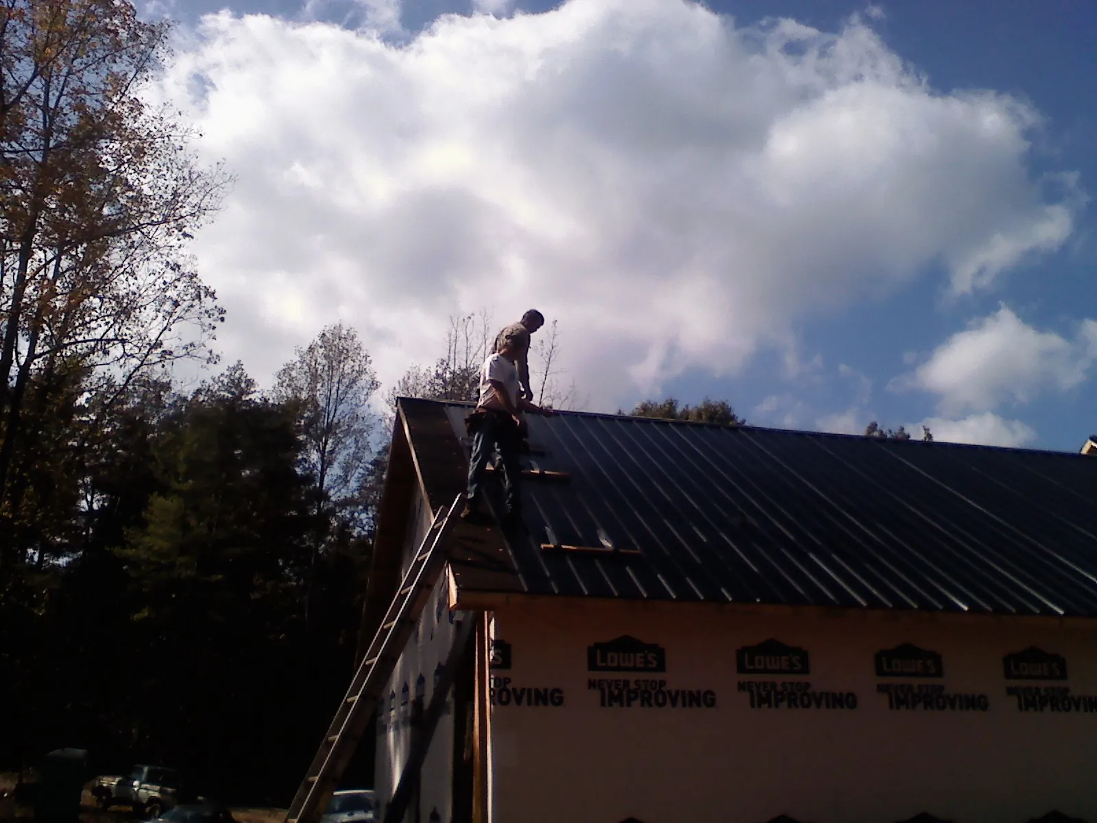 Roofer fastening dark metal panels high against a cloudy sky, from a Roof Inspection job in Cranford