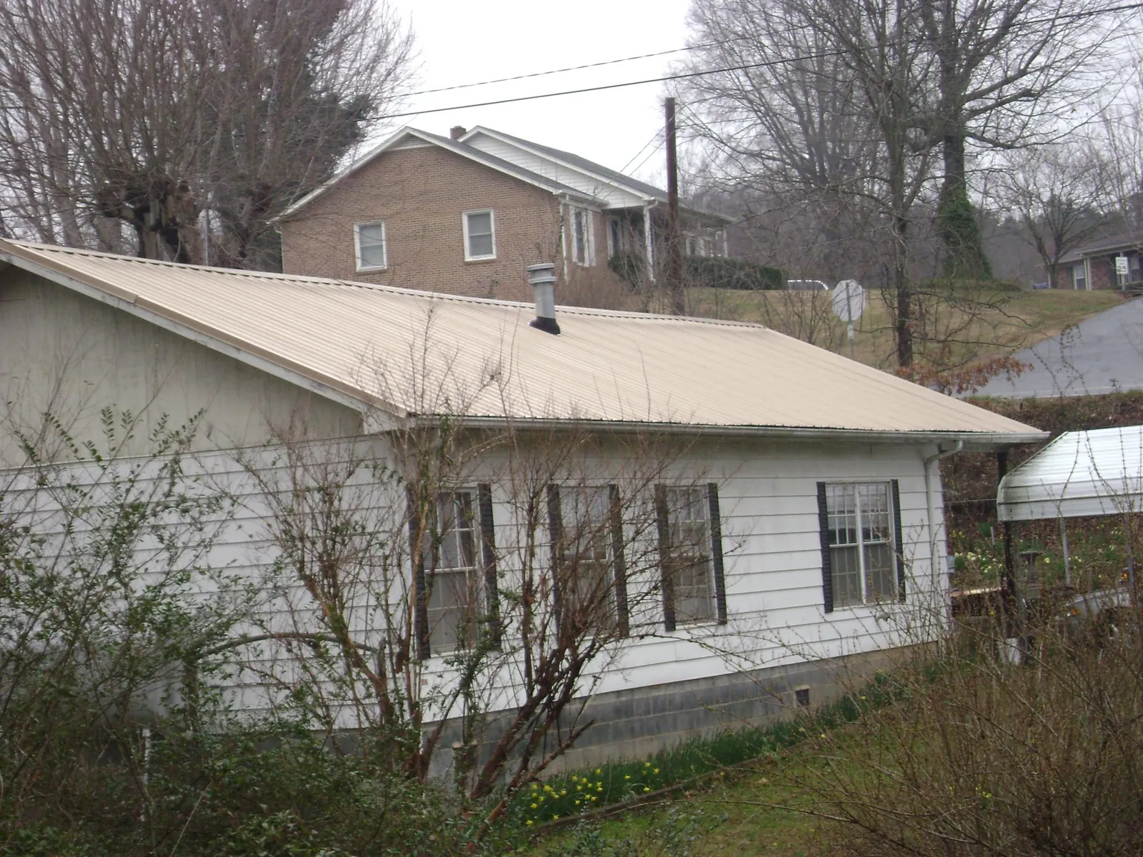 Tan metal roof on a white sided house set into a hillside — Commercial Roofing by Roofing Brothers in Cranford